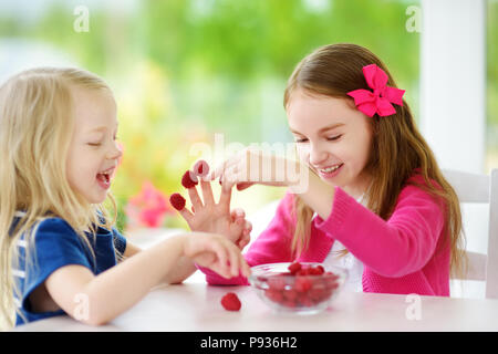 Due graziose bambine di lamponi di mangiare a casa. Carino bambini godendo il loro sani e freschi organici di frutti e bacche. Bambini divertirsi insieme. Foto Stock