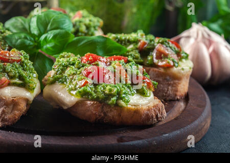 Bruschetta con pesto fresco, mozzarella e pomodori ciliegia sul bordo di taglio Foto Stock