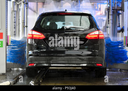 Auto va in car wash con un sacco di schiuma, blu di rotazione delle spazzole e i fari sono accesi Foto Stock