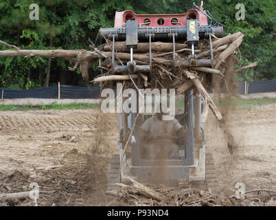 Stati Uniti Air Force Staff Sgt. James Barnes, membro dell'166Ingegnere Civile Squadron, Delaware Air National Guard, scuote lo sporco in eccesso fuori il legno utilizzando la benna alle prese di una minipala caricatrice che trasporterà il legno per un altro palo per la masterizzazione, come parte di una fase di costruzione di Camp Kamassa in Crystal molle, Mississippi, luglio 11, 2018. Camp Kamassa saranno stati prima completamente accessibile ai portatori di handicap, anno camp agevolazione per gli adulti e per i bambini con bisogni speciali, che viene costruito su 326 acri capeggiate dal Dipartimento della Difesa prontezza innovativo programma di formazione. Foto Stock