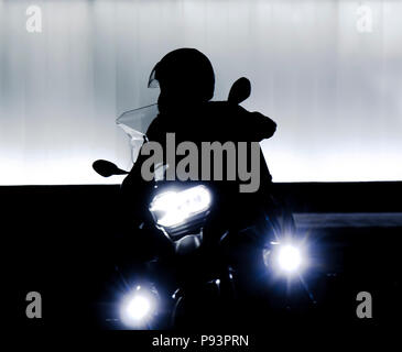 Sfocata silhouette di una persona uscire su una moto di fronte all edificio moderno in sella a una motocicletta con faro su nella notte in bianco e nero e w Foto Stock