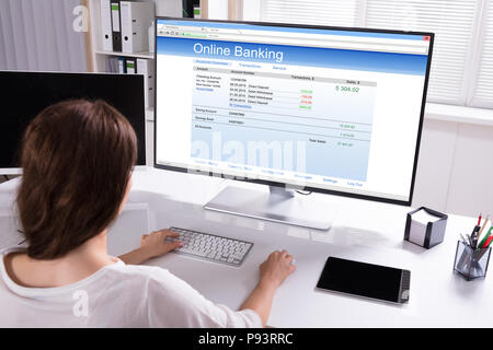 Vista posteriore di una imprenditrice facendo il banking online sul computer in ufficio Foto Stock