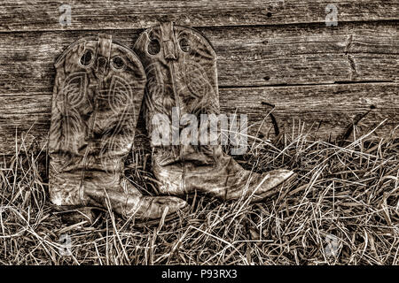 Paio di stivali da cowboy, nell'erba, appoggiata contro una parete weatherd. Foto Stock