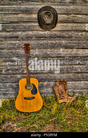 Acoutic guitar, cappello da cowboy, stivali da cowboy e vecchio, invecchiato farm shed parete. Rural Alberta, Canada. Foto Stock