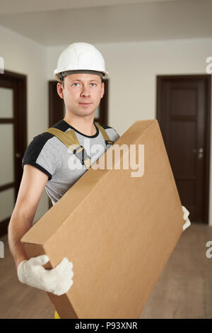 Uomo in hard hat tenere la scatola di cartone all'interno di casa Foto Stock