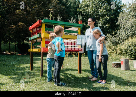 Insegnante spiegare un argomento ambientale su erbe a un piccolo gruppo di studenti primari. Apprendimento Outdoor - i bambini a discutere con un insegnante. Foto Stock