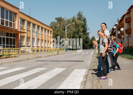 Madre andare a scuola a piedi con i suoi figli insegnando loro la sicurezza stradale. I bambini sul loro modo a scuola in attesa in un crosswalk. Foto Stock