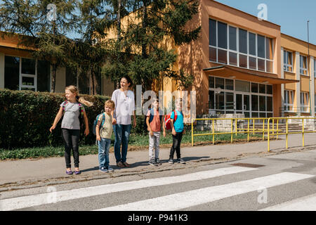 I bambini in attesa presso un attraversamento pedonale con la loro madre a guardare fuori per automobili. Madre per insegnare ai bambini la sicurezza stradale. Foto Stock