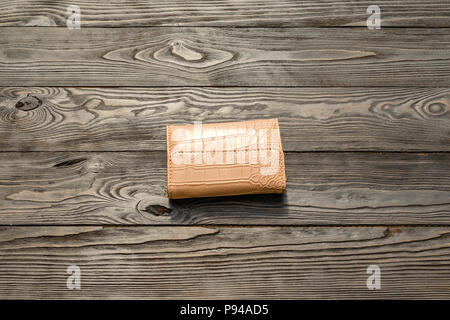 Pelle marrone con eleganza femminile sul portafoglio di legno scuro dello sfondo. Un singolo oggetto. Foto Stock