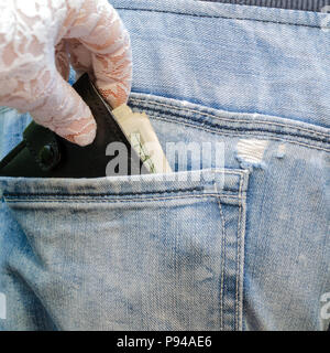 La mano in un guanto bianco tira fuori un portafogli con denaro, che sporge dalla tasca posteriore dei jeans blu. Il concetto di carefree. Per instagram format Foto Stock