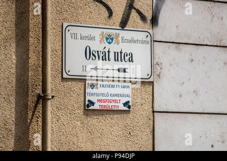 Un cartello stradale su una parete di un edificio a Budapest per Osvat utca con graffiti vicino ad essa Foto Stock