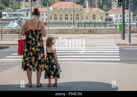 Una madre e figlia di adattamento che indossa abiti sun attendere per attraversare la strada sulle rive del Danubio a Budapest, Ungheria. Foto Stock