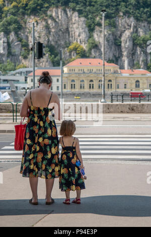 Una madre e figlia di adattamento che indossa abiti sun attendere per attraversare la strada sulle rive del Danubio a Budapest, Ungheria. Foto Stock