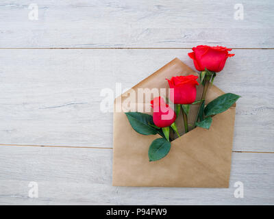 Busta di carta Kraft, con fiori rose rosse su fondo in legno, spazio per il testo, come congratulazioni matrimoni, compleanni. Foto Stock