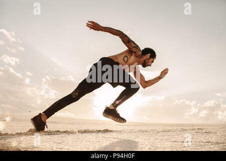Giovane atleta maschio lanciando off per una corsa sulla sabbia del deserto. Runner in esecuzione sulla duna di sabbia. Foto Stock