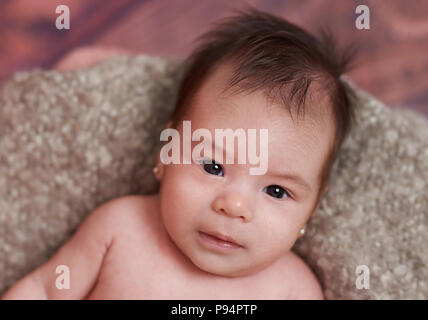 Ritratto di piccola bambina posa su grigio Sfondo coperta Foto Stock