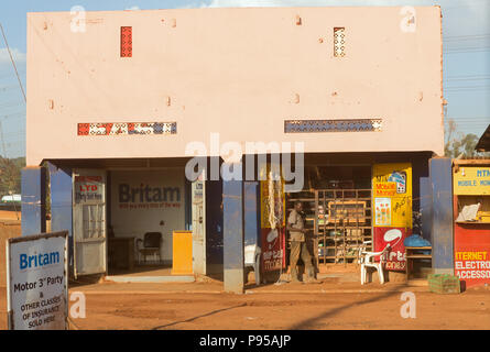 Wakiso Town, Uganda - Scene di strada. Un uomo fuma una sigaretta nella luce della sera davanti a un negozio. Foto Stock