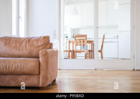 Appartamento interno di un soggiorno con pavimento in legno e un divano e cucina in background Foto Stock