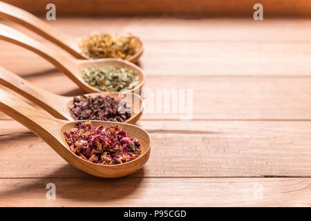 Cucchiai di legno con diverse erbe per infusione, in stile rustico, su sfondo di legno. Foto Stock