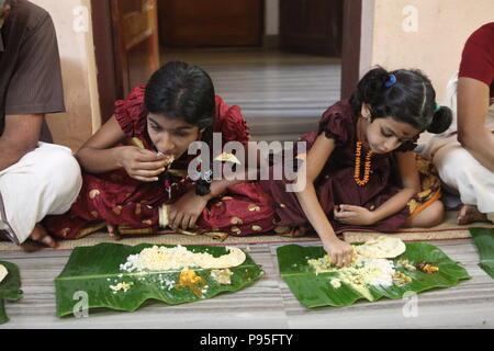 Una famiglia in kerala godendo di una festa in stile tradizionale,seduto sul pavimento,cibo servito su foglie di banana Foto Stock