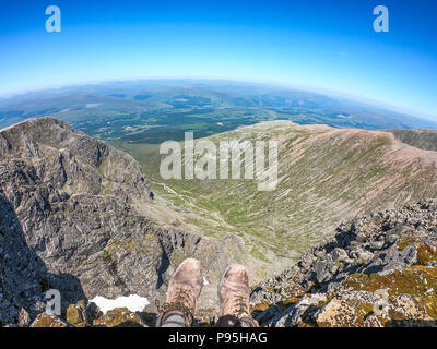 Un escursionista si siede con le gambe penzolanti off sul bordo della vetta del monte più alto nel Regno Unito. Ben Nevis sorge a 1345 metri abov Foto Stock