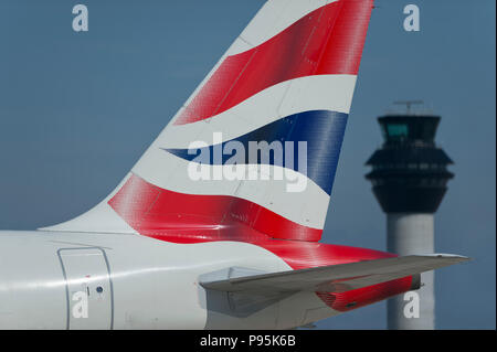 Il tailfin di British Airways Airbus A319-131 rullaggio lungo la pista di fronte alla torre di controllo dell'aeroporto di Manchester. Foto Stock
