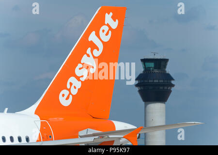 Il tailfin di Easyjet Airbus 319-111 rullaggio lungo la pista di fronte alla torre di controllo dell'aeroporto di Manchester. Foto Stock