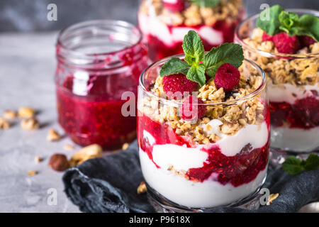 Yogurt parfafait con muesli, marmellata di lamponi e nel vasetto di vetro. Foto Stock