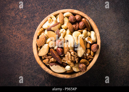 Assortimento di dadi in ciotola di legno scuro sul tavolo di pietra. Anacardi, nocciole, noci, mandorle, noci brasiliane e pinoli. Vista da sopra con copia spazio. Foto Stock