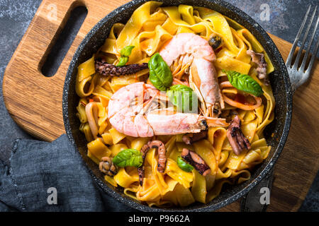 Pasta con frutti di mare. Tagliatelle con calamari, gamberi, polpo e cozze in salsa di pomodoro. Vista dall'alto sulla pietra nera tabella. Foto Stock