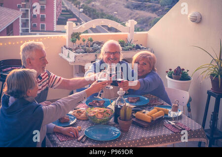 Gruppo di adulti caucasici persone mature a mangiare e a bere insieme celebrando caso di notte sul tetto con città e natura vista. estate un Foto Stock