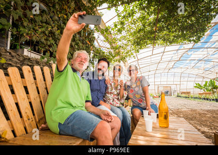 Famiglia con madre padre figlio e la moglie di stare insieme in attività per il tempo libero in un luogo naturale seduto su una panca di legno. prendere un selfie con la nuova smart Foto Stock