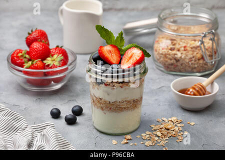 Dieta sana prima colazione. muesli, yogurt, mirtilli , le fragole in un recipiente su un cemento grigio Sfondo. spazio copia Foto Stock