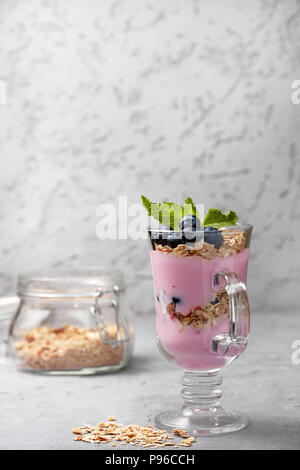 Yogurt con muesli, mirtilli, banana in un bicchiere per una sana prima colazione. Foto Stock