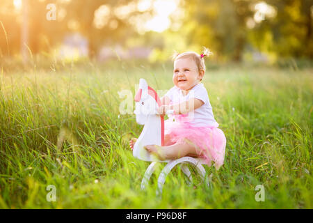 Bellissima bambina in abito rosa a cavallo di legno cavallo giocattolo all'aperto Foto Stock