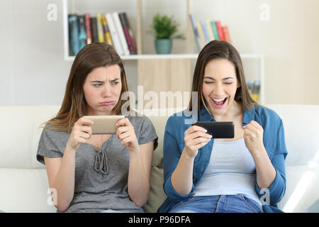 Vista frontale ritratto di un perdente invidiosi ragazza guardando il suo vincitore amico seduto su un divano nel salotto di casa Foto Stock