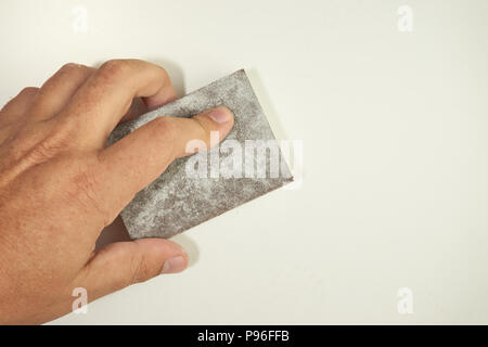 Vista ravvicinata di una carteggiatura a mano il muro con una spugna per levigatura isolato su bianco. Utensili abrasivi, bricolage, copia dello spazio. Foto Stock