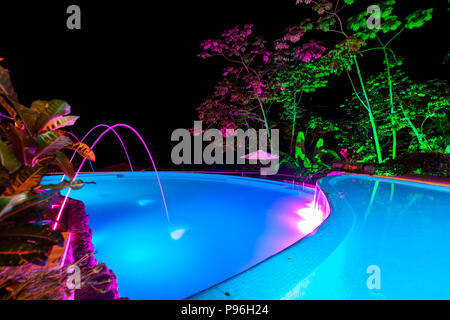 Una tranquilla piscina con luci incandescenti riflettendo su alberi tropicali attorno ad esso con una notte buia sky in Costa Rica. Foto Stock