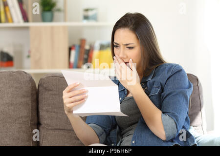 Triste lettura donna cattiva notizia in una lettera su carta seduta su un divano nel salotto di casa Foto Stock