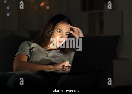 Ritratto di una donna preoccupati usando un computer portatile nella notte a casa Foto Stock