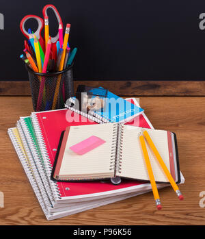 Quaderni scolastici e gli accessori su una scrivania di legno con una lavagna vuota in background Foto Stock