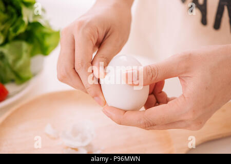 Mani femminili è bombardare le uova di gallina. La donna si prepara la colazione a casa. Bollite le uova di gallina in legno ware al buio su un tavolo. Tonificazione vintage Foto Stock