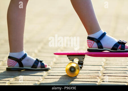 Bambino gambe slim in calze bianche e sandali nero sulla plastica rosa su skateboard luminosa estate copia sfocata spazio sullo sfondo della pavimentazione. All'aperto ac Foto Stock