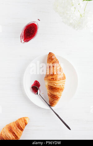 Croissant, marmellata e fiore bianco sul tavolo di legno. Tradizionale prima colazione francese. Vista dall'alto. Foto Stock