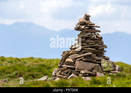 Illuminato da Bright sole estivo irregolare pietre di montagna impilati e bilanciati come pyramid pila sulla verde valle erbosa sulla luce bianco-blu di spazio copia sky backg Foto Stock