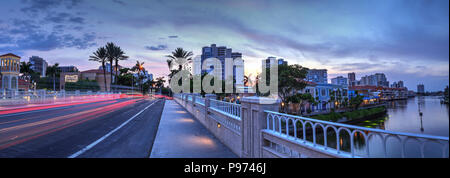 Naples, Florida, Stati Uniti d'America - 14 Luglio 2018: auto sentieri di luce lungo la strada come il tramonto ascende al di sopra del colorati negozi del villaggio su Venetian Bay in Foto Stock