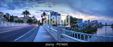 Auto sentieri di luce lungo la strada come il tramonto ascende al di sopra del colorati negozi del villaggio su Venetian Bay in Naples, Florida Foto Stock