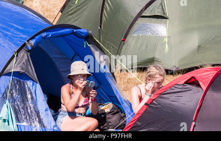 Due giovani frequentatori del festival, seduta in area camping, ottenere pronto per l'ultimo giorno del festival, Latitude Festival, Henham Park, Suffolk, Inghilterra,15 Luglio, 2018 Foto Stock