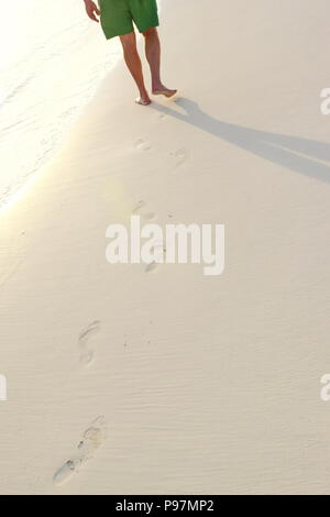 Senior uomo a camminare sul Treasure Cay Beach la mattina presto sulla sabbia incontaminata con il sorgere del sole. Orme nella sabbia. Foto Stock