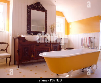 Giallo roll top bagno in un giallo e stanze da bagno di colore bianco con un raffinato specchio sopra un armadio impostato con doppi lavandini Foto Stock